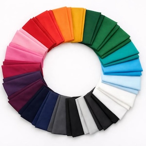May include: A circular arrangement of folded fabric squares, displaying a wide range of colours. The spectrum includes red, orange, yellow, green, blue, and violet hues. The fabric is set against a white backdrop, emphasizing the colour diversity.