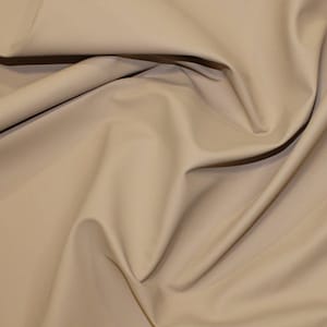 May include: A close-up of a beige fabric with a smooth texture. The fabric is folded and draped, showing its soft and supple quality.
