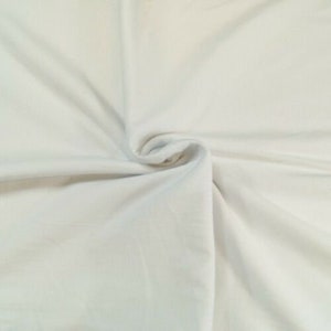May include: A close-up of a white fabric with a smooth texture. The fabric is folded and draped, showing its soft and flowing nature.