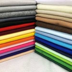 May include: A collection of folded felt fabric sheets arranged in two stacks. The left stack features shades of grey, black, red, yellow, orange, pink, and purple. The right stack displays white, cream, tan, brown, blue, and green colour variations.