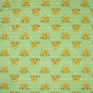 May include: A green and white striped fabric with a repeating pattern of yellow cartoon faces. The faces have green skin, large eyes, and a wide smile.