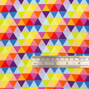 Op de afbeelding: Een kleurrijke stof met een geometrisch patroon van herhalende driehoeken in tinten geel, oranje, rood, roze, paars, blauw en lichtblauw. Een liniaal ligt op de stof en toont de afmetingen in inches.