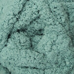 May include: Close-up of a soft, textured fabric in a muted teal color. The material has a plush, looped appearance, suggesting a cozy texture. The fabric's surface is densely packed with small, irregular loops, creating a tactile and visually appealing surface.