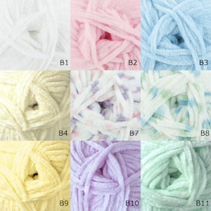 K&ouml;nnte beinhalten: Eine Sammlung von 11 Garnkn&auml;uel in verschiedenen Farben, darunter Wei&szlig;, Rosa, Blau, Gelb, Lavendel und Gr&uuml;n. Das Garn ist weich und flauschig mit einer flauschigen Textur.