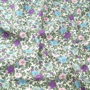 May include: White fabric with a floral pattern featuring small blue, pink, and purple flowers on a white background.