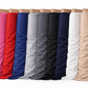 Puede incluir: Una colección de rollos de tela en varios colores, incluyendo rosa, rojo, azul, gris, negro, azul marino, blanco y beige. Cada rollo está montado sobre una base de madera, mostrando los diferentes tonos y texturas del material.
