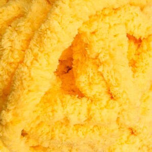 May include: Close-up of a pile of soft, yellow yarn. The yarn has a fluffy, textured appearance, with visible strands and a dense, plush feel. The color is a bright, sunny yellow, with variations in tone creating depth and dimension.