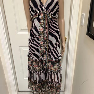 May include: A sleeveless midi dress with a V-neckline and spaghetti straps. The dress features a black and white striped pattern on the bodice and a floral print on the skirt. A matching floral sash ties at the waist. The dress has a tiered skirt.