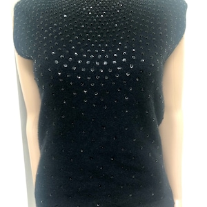 May include: A black sleeveless sweater with a high neckline and a pattern of small black sequins.