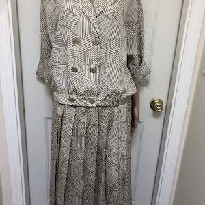 May include: A beige and white geometric print dress with a double-breasted button closure and a pleated skirt.