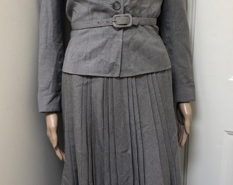 May include: A grey skirt suit with a pleated skirt and a jacket with a belt. The jacket has five buttons and a pointed collar.