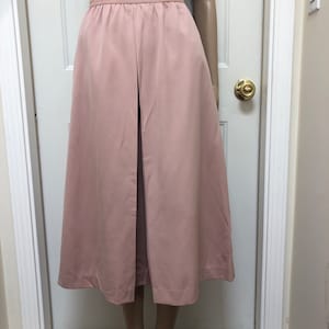 May include: A dusty rose-colored midi skirt with a high waist and a center front slit. The skirt is made of a smooth, silky fabric.