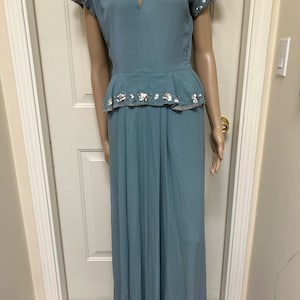 Könnte beinhalten: Ein langes, hellblaues Kleid mit V-Ausschnitt und kurzen Ärmeln. Das Kleid hat ein tailliertes Oberteil und einen fließenden Rock. Die Ärmel und die Taille sind mit silbernen Pailletten verziert.