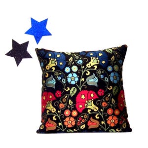 May include: Square decorative pillow with a black background and a colorful floral pattern. The flowers are red, blue, orange, and yellow. Two glittery star-shaped decorations are in the upper left corner.