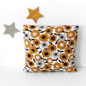 May include: A white pillow with a floral pattern in shades of mustard yellow, black, and gray. The flowers are stylized and resemble large daisies.