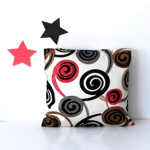 May include: A white throw pillow with a geometric pattern of black, red, and brown swirls.