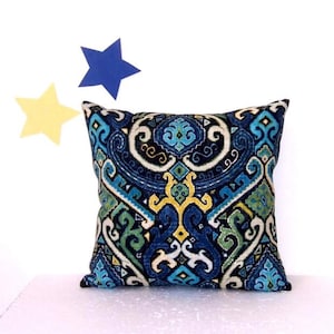 May include: A square throw pillow featuring a dark blue, light blue, green, and yellow intricate damask pattern. The fabric has a textured appearance with symmetrical swirling motifs and geometric shapes covering the entire front surface.