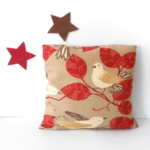 May include: A beige throw pillow with a red and white bird and leaf pattern. The pillow has a brown linen-like texture.