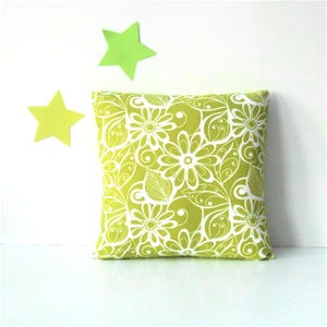 May include: Square decorative pillow with a lime green floral pattern. The pillow features white flowers, leaves, and swirls on a green background. Two lime green star-shaped decorations are on the white background.