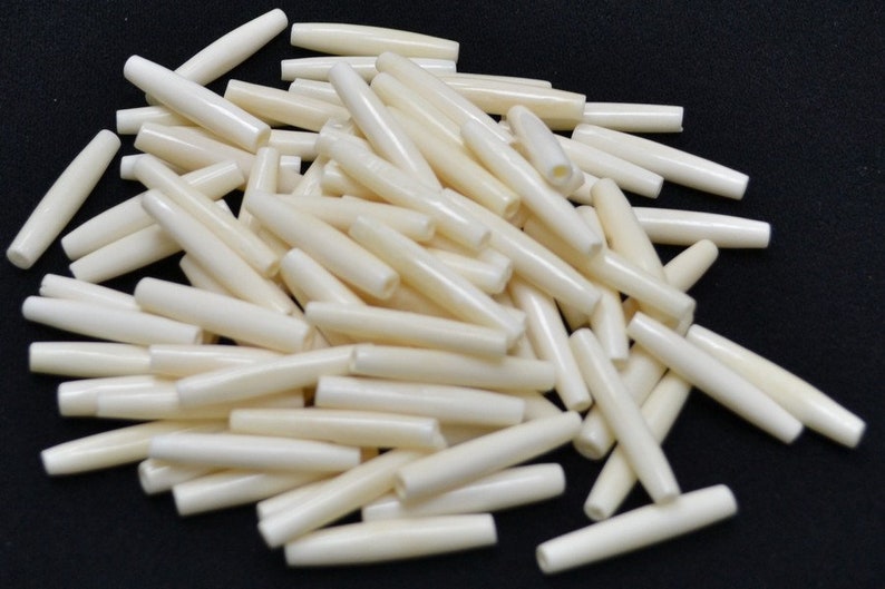 Peut inclure: Un tas de perles cylindriques lisses de couleur blanc cass&eacute;. Les perles mesurent environ 2,5 cm de long et ont une extr&eacute;mit&eacute; l&eacute;g&egrave;rement arrondie.