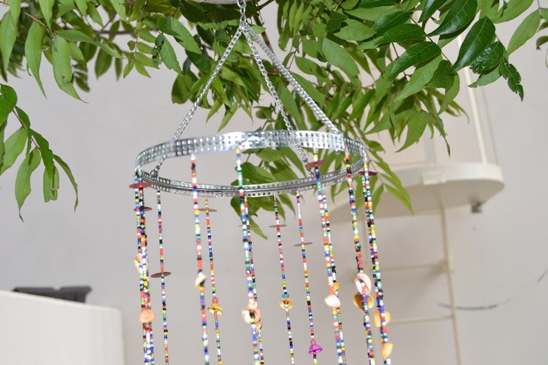 May include: A colorful beaded wind chime with shells hanging from a silver metal ring. The wind chime is suspended from a silver chain.