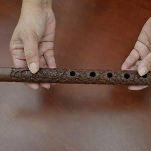 May include: A brown wooden flute with intricate carvings and six finger holes.