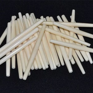 May include: A pile of approximately 40 off-white bone beads, each about 2 inches long and slightly tapered at one end.