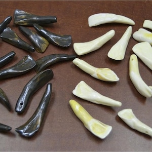 May include: An assortment of carved, dark gray and off-white bone or horn pendants. The pendants are in various shapes, including curved and pointed designs. Some have a hole drilled for stringing.