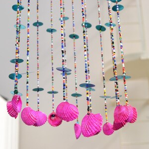 May include: A colorful beaded mobile with pink seashells hanging from strings of beads. The mobile has blue, green, red, white, and black beads.