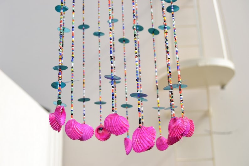 May include: A colorful beaded mobile with pink seashells hanging from strings of beads. The mobile has blue, green, red, white, and black beads.