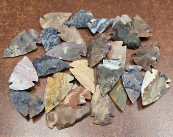 Puede incluir: Una colección de puntas de flecha de piedra de diversas formas y tamaños, con una gama de colores que incluye beige, gris, marrón y blanco con patrones jaspeados, moteados y veteados en las superficies de piedra tallada y texturizada.
