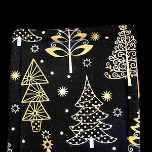 May include: A square fabric coaster featuring a black background with a gold metallic print of stylized Christmas trees, stars, and foliage. The edges are stitched with a thick border, creating a quilted appearance on the textile surface.
