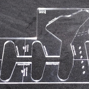 May include: A clear plastic template with multiple cutouts for different shapes and sizes. The template includes measurements in millimeters for depth and width. The template is designed for woodworking projects.