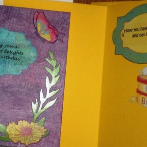 Może przedstawiać: Fioletowa kartka z niebiesko-białym wzorem kwiatowym i tekstem "Wishing you a bouquet of delights on your birthday". Kartka jest otwarta, aby ujawnić ż&oacute;łtą kartkę z zielono-białą ramką i tekstem "Hope you have your cake and eat it too!" oraz kresk&oacute;wkowym psem trzymającym tort z napisem "Happy Birthday".