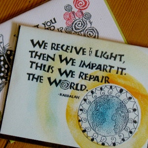 May include: A green card with a yellow and orange watercolor background. The card features a black and white illustration of a globe with a quote that reads "We receive the light, then we impart it. Thus we repair the world. -Kabbalah"