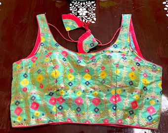 May include: A turquoise and pink embroidered blouse with a geometric pattern. The blouse has a scoop neck and sleeveless design. It comes with two matching fabric ties.