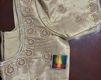 May include: A gold embroidered blouse with intricate beading and embellishments. The blouse has a round neckline and short sleeves.
