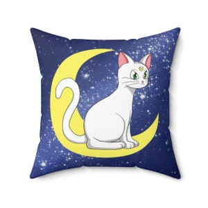 May include: A blue pillow with a white cat sitting on a yellow crescent moon. The background is a dark blue with white stars.