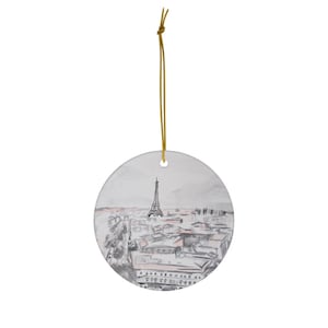 May include: A white ceramic ornament with a watercolor illustration of the Eiffel Tower and the Parisian skyline. The ornament is round and has a gold string for hanging.