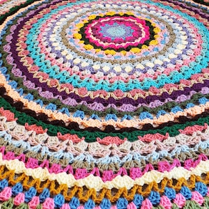 May include: A colourful crocheted round rug with multiple layers of different coloured yarn. The rug has a circular pattern with a centre circle of pink, purple, and blue yarn.