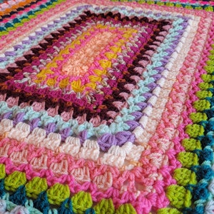 May include: A colourful crocheted blanket with a rectangular shape and a variety of bright colours, including pink, green, blue, and yellow.