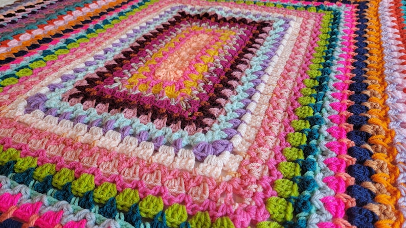 May include: A colourful crocheted blanket with a rectangular shape and a variety of bright colours, including pink, green, blue, and yellow.