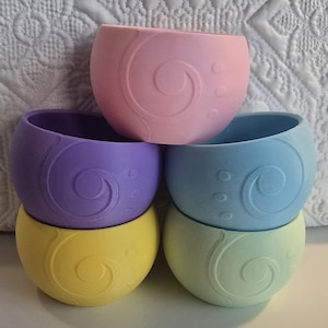 May include: Set of four pastel colored silicone bowls with a swirl design. The bowls are stacked in a pyramid shape, with the pink bowl on top and the green bowl on the bottom.