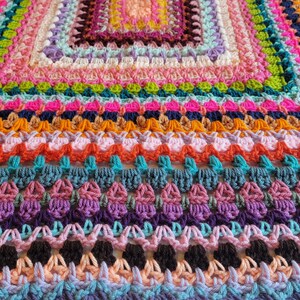 May include: A colourful crocheted blanket featuring a range of stitches and colours, including pink, orange, green, blue and purple.