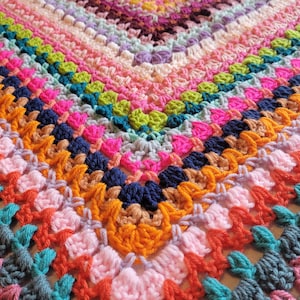 May include: A colourful crocheted blanket featuring a range of bright colours, including pink, orange, green, blue, and purple. The blanket is crafted with a textured stitch that creates a unique and interesting pattern.
