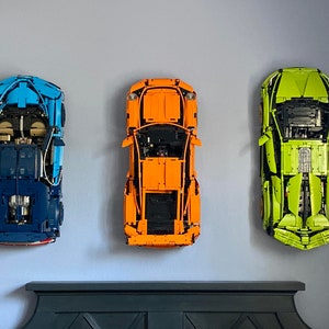 Może przedstawiać: Trzy modele samochod&oacute;w Lego wystawione na ścianie. Samochody to niebieski Bugatti Chiron, pomarańczowe Porsche 911 GT3 RS i zielony Lamborghini Aventador SVJ.