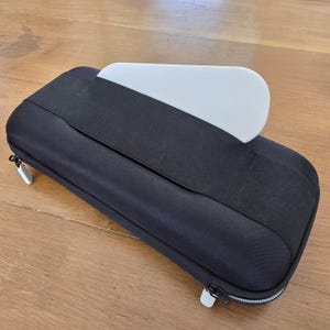 Op de afbeelding: Een zwarte draagtas met rits en een witte inzet voor een draagbaar apparaat. De tas heeft een textuur van stof aan de buitenkant en een ritssluiting.