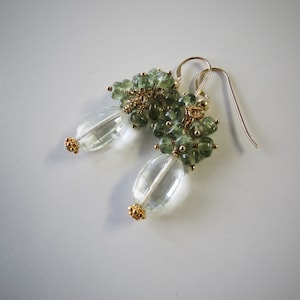 May include: A pair of earrings with green gemstone clusters and clear teardrop-shaped crystals hanging from gold-toned hooks.