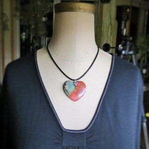 May include: A black necklace with a heart-shaped pendant made of red, orange, and green stone.