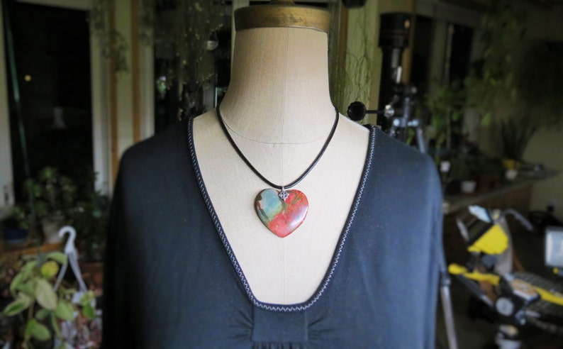 May include: A black necklace with a heart-shaped pendant made of red, orange, and green stone.
